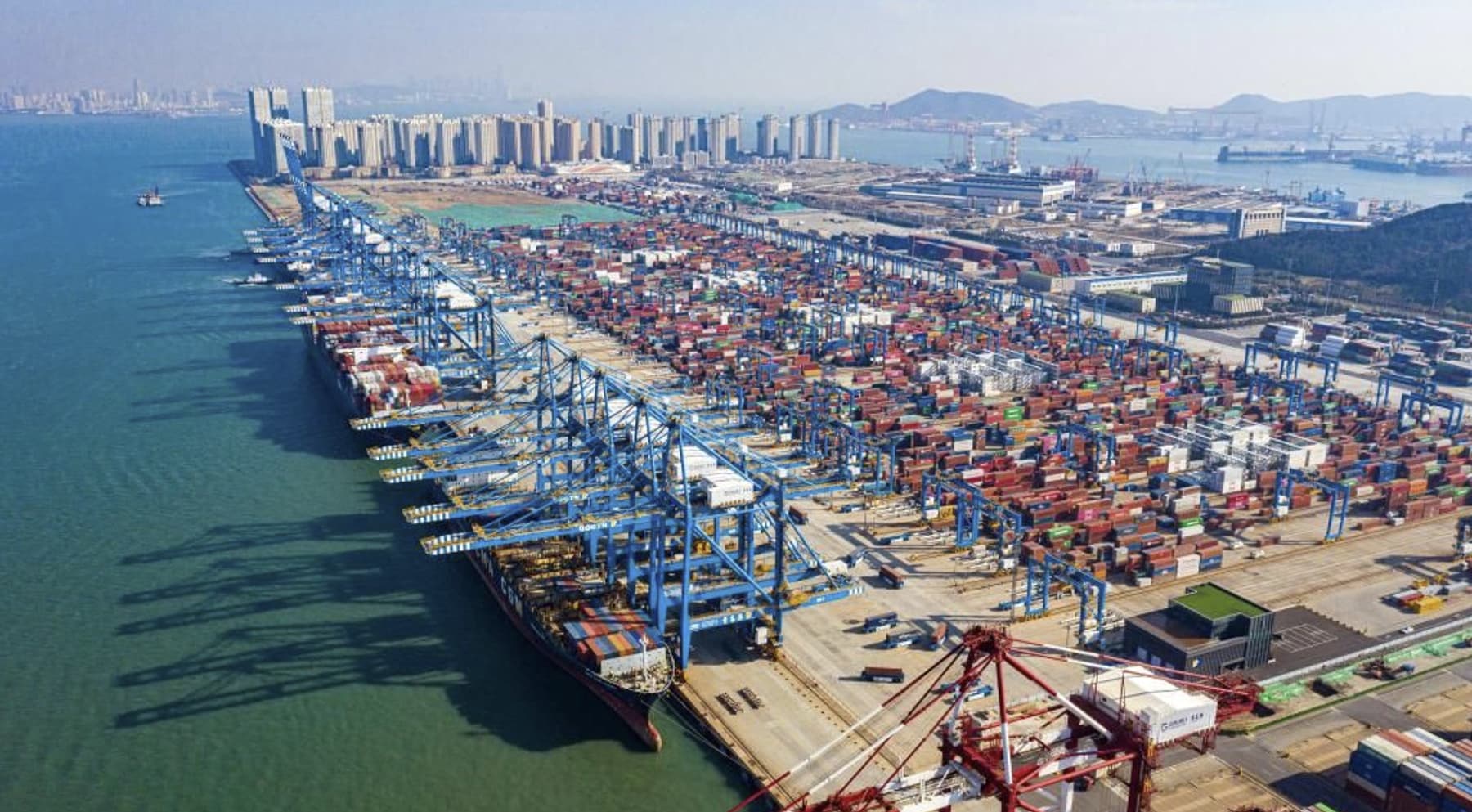 Aerial view of a container terminal, with gantry cranes working vessels alongside stacked container yards